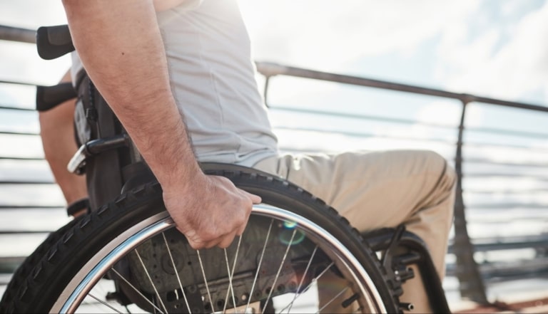 Hand und Arm von einem Mann, der im Rollstuhl sitzt, bewegen das Rad am Rollstuhl.