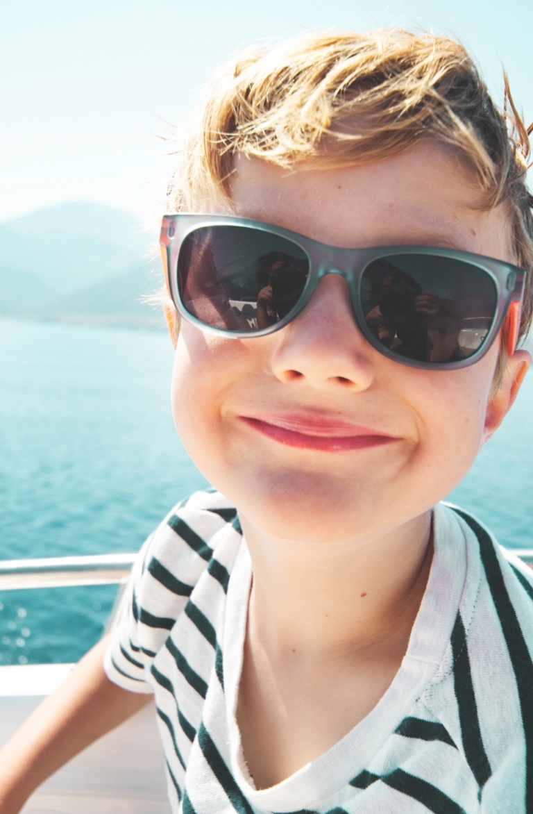Ein Junge mit Sonnenbrille und T-Shirt an Bord der MS Mondseeland schaut lustig.
