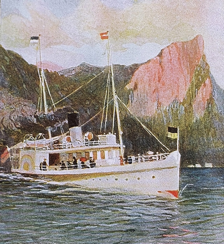 Ein farbenfrohes Aquarell zeigt das Dampfschiff Habsburg in Fahrt auf dem Mondsee. Schwarzer Rauch kommt aus dem Schornstein. Im Hintergrund ist die Drachenwand und im Vordergrund ein Ruderboot mit drei Personen zu sehen. Die Szene spielt gegen Ende des 19. Jahrhunderts.