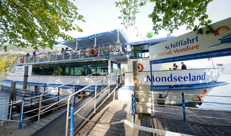 Der Anlegesteg des Passagierschiff MS Mondseeland an der Seepromenade in Mondsee. Es ist ein sonniger Sommertag im Jahr 2015. Passagiere sind schon an Bord. Rechts steht das Schild mit der Aufschrift Schifffahrt Meindl Mondsee.