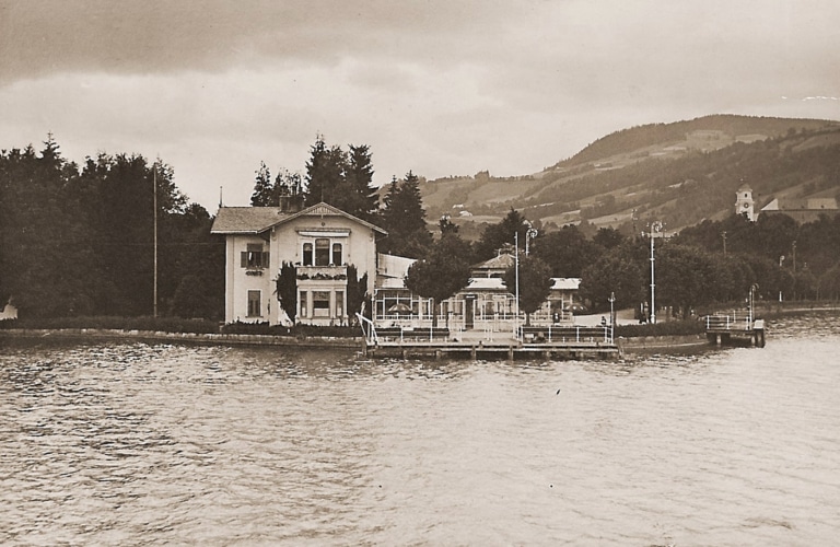 Die Seevilla mit den Schiffsanlagen in Mondsee vom See aus. Ein Schwarzweiß-Foto rund um das Jahr 1910.