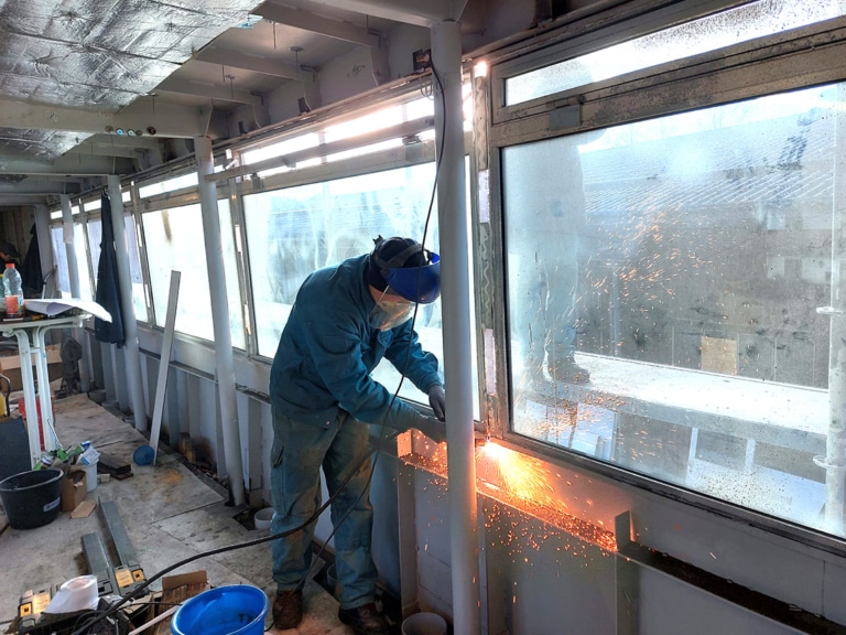 Schweißarbeiten an bei der Schiffsrestauration vor einer Fensterscheibe