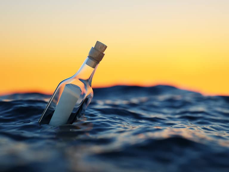 Eine Flaschenpost treibt auf dem Wasser. Man sieht einen Brief in der Flasche. Das Wasser ist dunkel, im Hintergrund ist ein Sonnenuntergang.